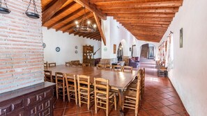 A spacious dining area with a long wooden table and chairs, a brick wall, and a wooden ceiling. - Molino del Alferez Sayalonga by Ruralidays (Málaga)