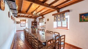 A spacious dining area with a long wooden table and chairs, a chandelier, and a rustic ceiling. - Molino del Alferez Sayalonga by Ruralidays (Málaga)