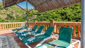 A terrace with sun loungers, a table with a bottle and glasses, and a view of green hills. - Molino del Alferez Sayalonga by Ruralidays (Málaga)