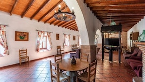 A spacious living room with a high wooden ceiling, a fireplace, a television, and a dining area with a round table and chairs. - Molino del Alferez Sayalonga by Ruralidays (Málaga)