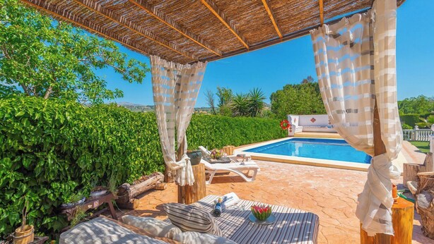Un espace aménagé au bord de la piscine, avec une pergola, des chaises longues et une petite table sur laquelle sont posés une bouteille et des fleurs.