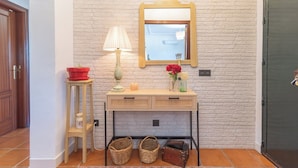 Un couloir avec une porte en bois, une petite table avec une lampe, un miroir et des paniers en osier.