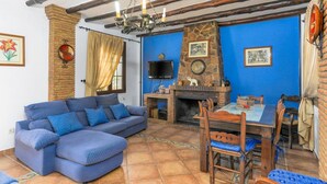 Un salon avec un canapé bleu, une cheminée, une table à manger avec des chaises et un téléviseur fixé au mur.