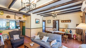Een gezellige woonkamer met een bank, fauteuil, houten balken en een eethoek met een tafel en stoelen.