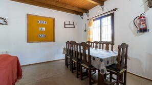 A dining area with a wooden table and chairs, a yellow sign with text, a window with curtains, and a fire extinguisher on the wall.