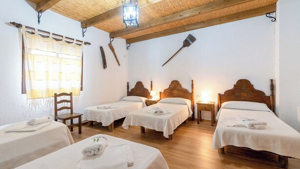 Una habitación con cuatro camas individuales, cabeceros de madera y techo rústico de madera.