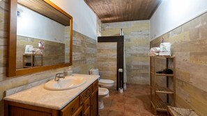 A bathroom with a wooden vanity, a sink, a mirror, a toilet, and a shower area. - Cortijo La Bodega - Conjunto Benaoján by Ruralidays (Málaga)