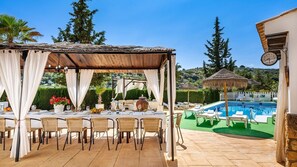Un espace extérieur aménagé pour les repas, avec une pergola couverte, une piscine et des chaises longues.