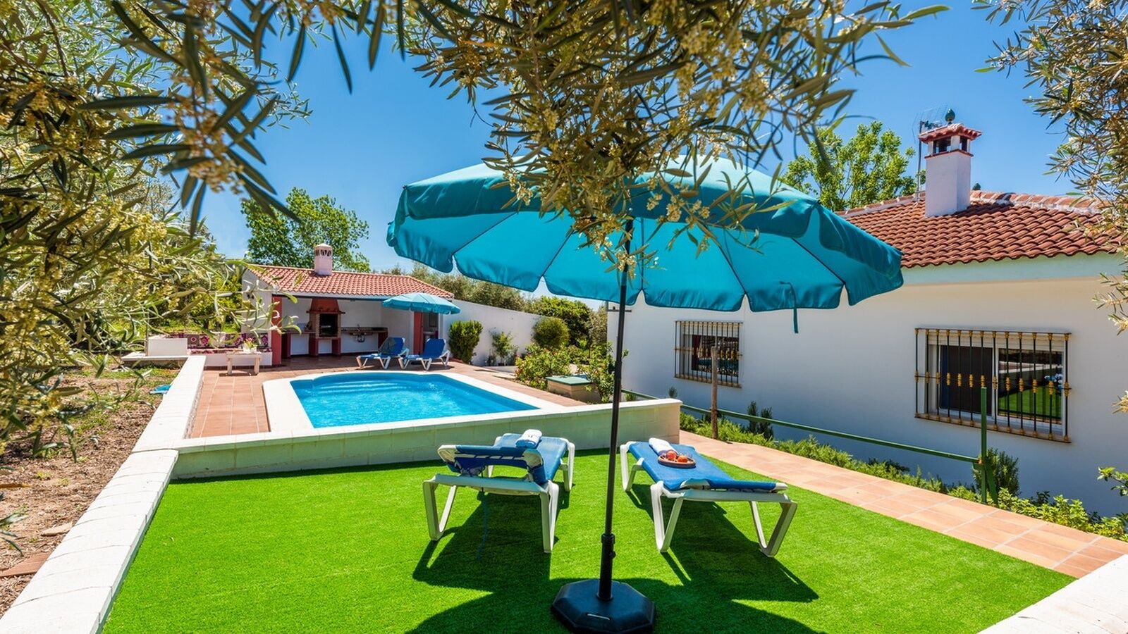 Patio trasero con piscina, dos sillones de descanso y una mesa con una bebida.