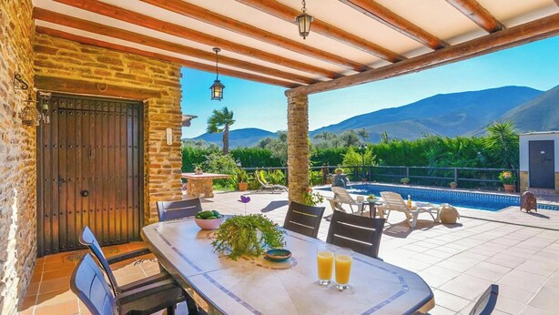 Ein überdachter Patio mit Pool, Steinmauern und Sitzgelegenheiten im Freien.