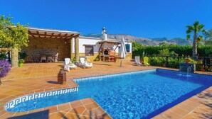 A swimming pool with a tiled edge, surrounded by lounge chairs and a patio area with a stone wall.