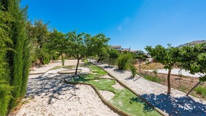 Um jardim ajardinado com caminhos, árvores e um céu azul claro.