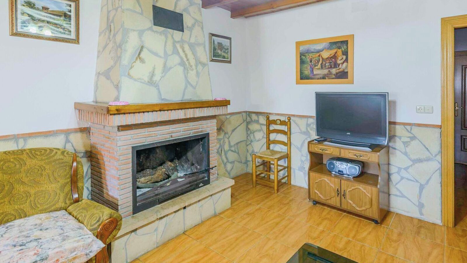 Una sala de estar con chimenea, un televisor sobre un mueble de madera, un sofá estampado y un sillón.