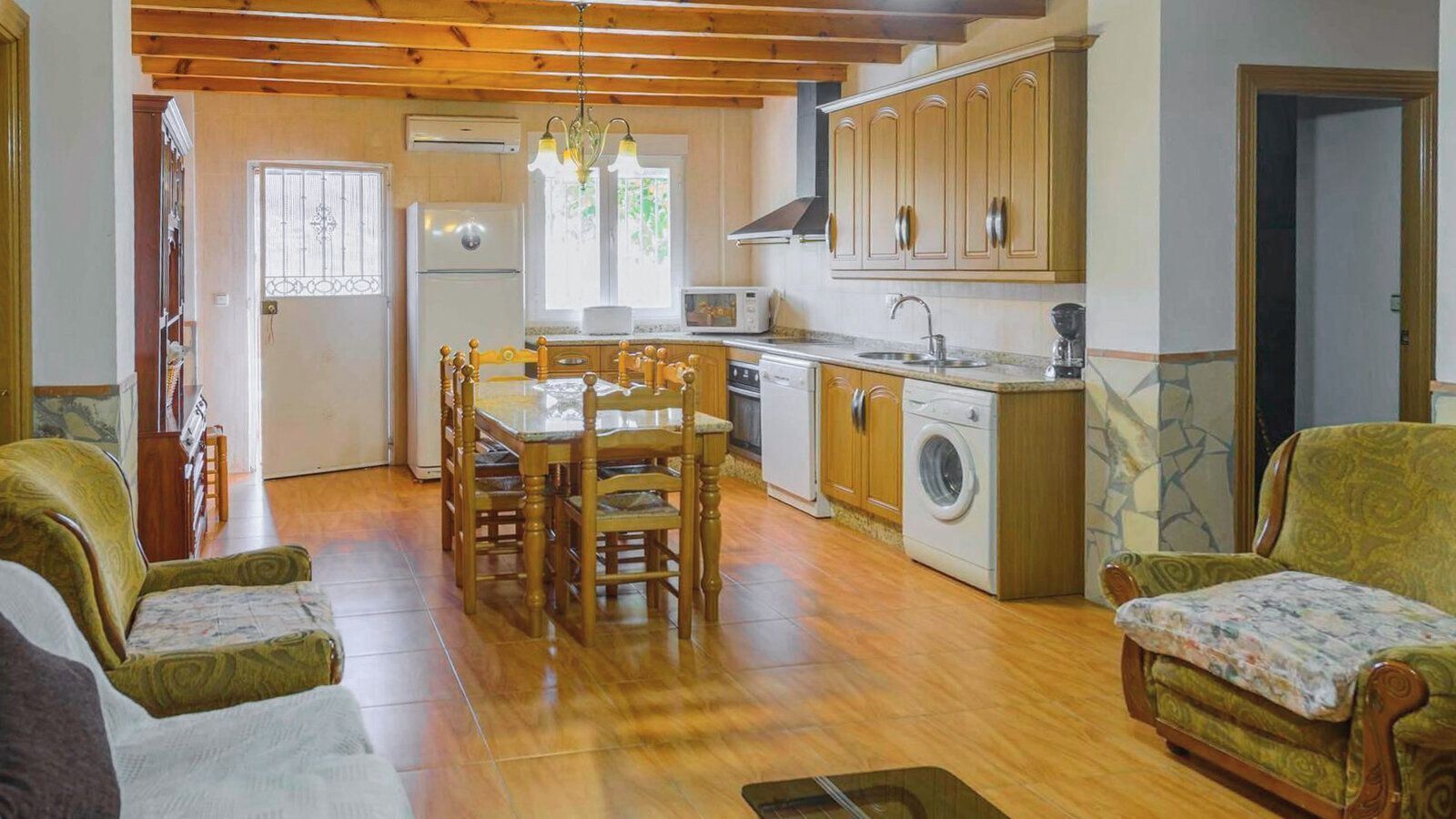 Una cocina acogedora con armarios de madera, una mesa de comedor y sillas. Hay una lavadora y un fregadero.