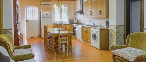 Una cocina acogedora con armarios de madera, una mesa de comedor y sillas. Hay una lavadora y un fregadero.