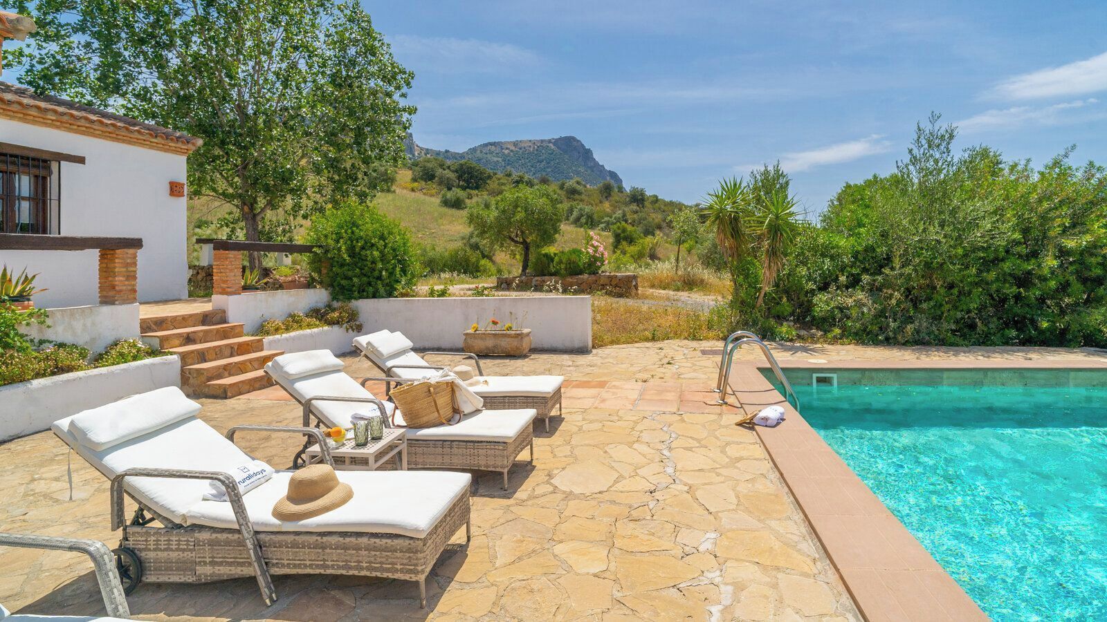 A poolside area with lounge chairs, a stone patio, and a view of a mountain.
