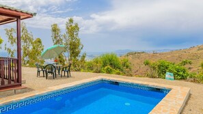Une piscine dont le fond est recouvert de carreaux formant un motif géométrique, entourée d’une terrasse avec une table et des chaises, et offrant une vue sur un paysage vallonné.