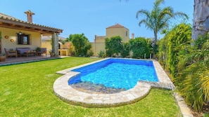 A swimming pool with stone edging, surrounded by a well-maintained lawn and various plants.