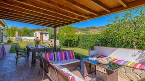 Eine Terrasse im Freien mit einer Holz-Pergola, Korbmöbeln und einer Steinmauer.