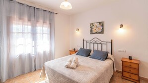 A neatly made bed with a white comforter and two pillows, a bedside table with a lamp, and a window with sheer curtains. - Casa Amelia Cómpeta by Ruralidays (Málaga)