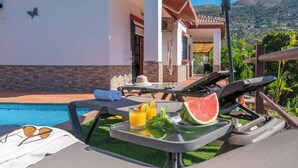 A poolside lounge area with a table set with a watermelon, glasses of orange juice, and sunglasses. - Casa Amelia Cómpeta by Ruralidays (Málaga)