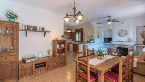 A cozy kitchen with wooden cabinets, a dining table with chairs, and a built-in stove. - Casa Amelia Cómpeta by Ruralidays (Málaga)