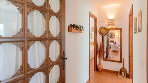A hallway with a wooden door with glass panels, a mirror, a vase with plants, and a shelf with decorative items.