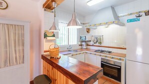 A kitchen with a wooden countertop, a gas stove, a sink, and hanging utensils.
