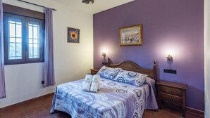 A bedroom with a bed, two wall-mounted lamps, a nightstand, a wooden dresser, and a window with curtains.