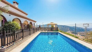 A swimming pool with a wooden fence, a gazebo, and a view of mountains.