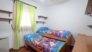 A bedroom with two bunk beds, a window with sheer curtains, and wall-mounted shelves.