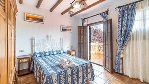 A bedroom with a bed, wooden beams, a window with curtains, and a view of the outside.