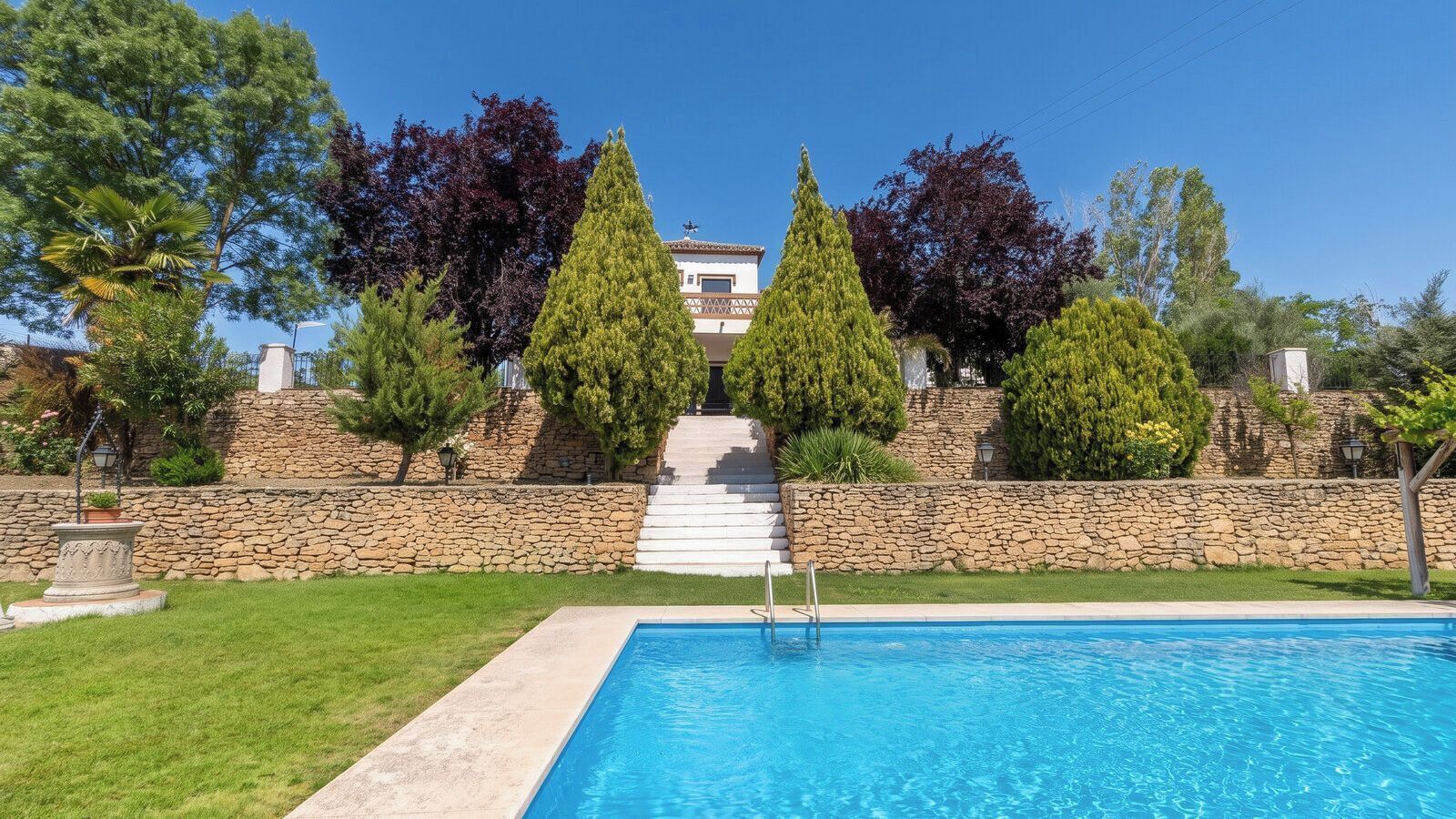 A swimming pool with a stone wall and steps leading to a building.