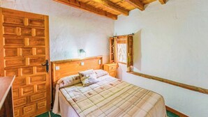 A bedroom with a wooden headboard, a bed with a quilt, a nightstand, a dresser, and a window with curtains. - Cortijo El Chinas Órgiva by Ruralidays (Granada)