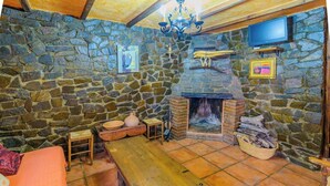 A stone-walled room with a fireplace, wooden furniture, and a television mounted on the wall. - Cortijo El Chinas Órgiva by Ruralidays (Granada)