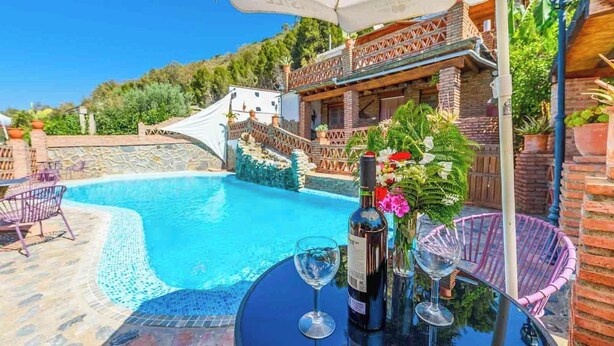 A pool area with a clear blue pool, a table with a bottle and glasses, and a chair. - Cortijo El Chinas Órgiva by Ruralidays (Granada)