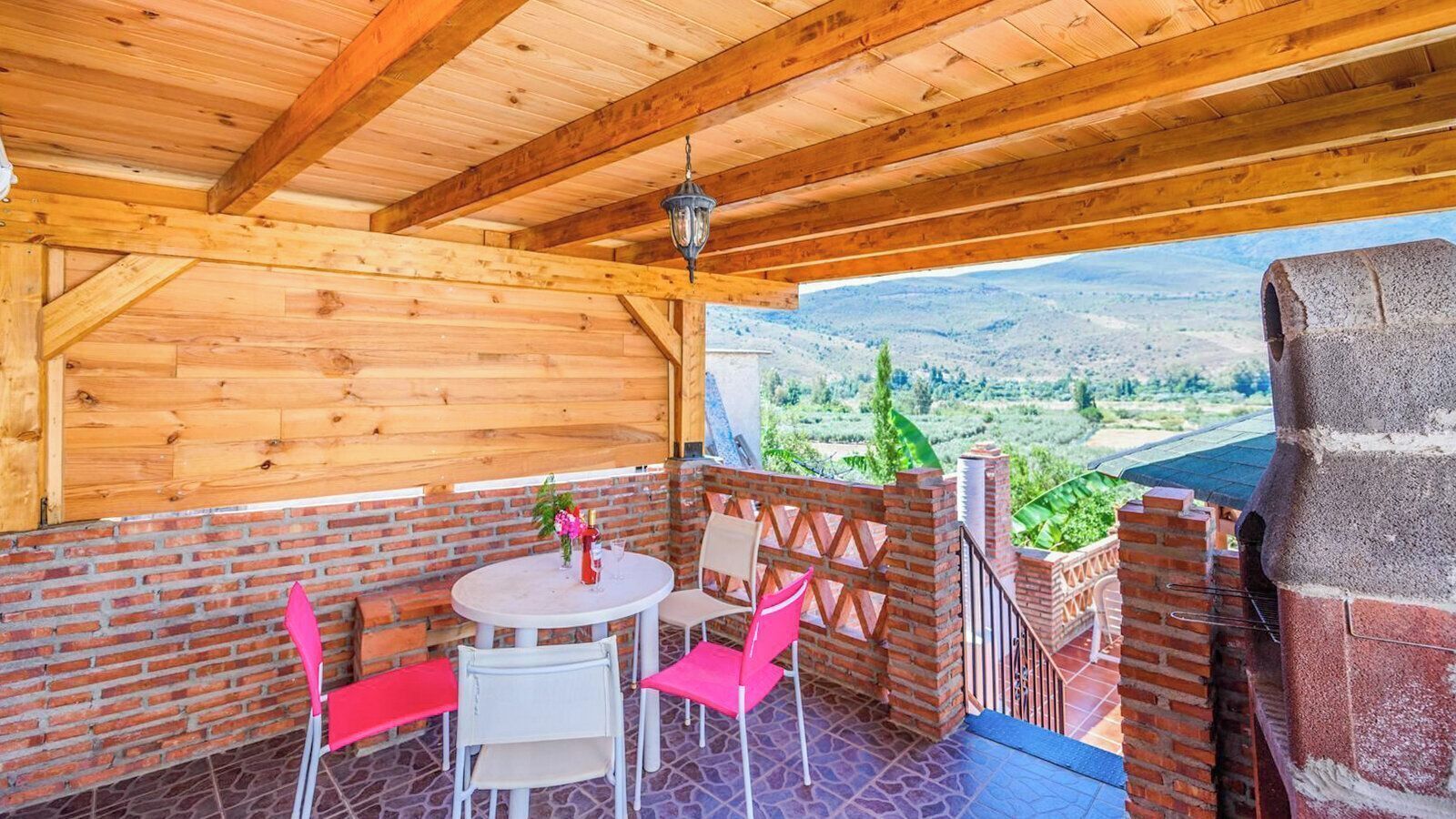 A covered patio with a brick wall, a round table with chairs, and a view of a valley.