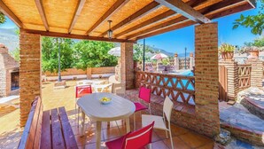 An outdoor patio with a wooden pergola, a round table with chairs, and a pool in the background. - Cortijo El Chinas Órgiva by Ruralidays (Granada)