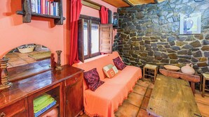 A cozy room with a stone wall, a wooden bench, a sofa with cushions, and a bookshelf with books. - Cortijo El Chinas Órgiva by Ruralidays (Granada)