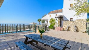 A wooden deck with a picnic table and a vase of flowers, overlooking a pool and a white building with stone walls. - Cuesta Blanca Montilla by Ruralidays (Córdoba)