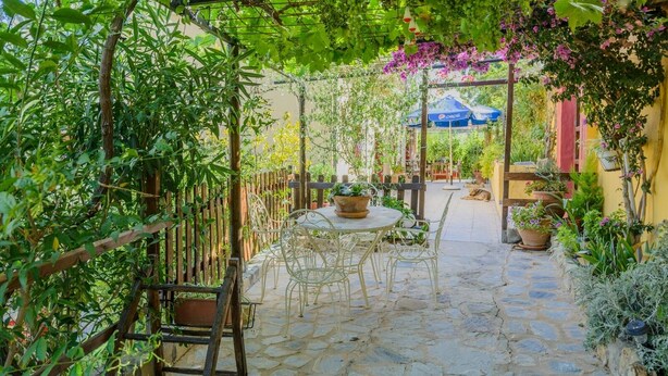 A stone-paved patio with a round table and chairs, surrounded by lush greenery and potted plants. - Cortijo San Jose Iznájar by Ruralidays (Córdoba)