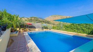 A swimming pool with a tiled edge, surrounded by potted plants and a red umbrella. - Cortijo San Jose Iznájar by Ruralidays (Córdoba)