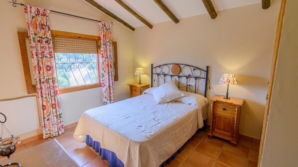 Un dormitorio con cama, dos mesitas de noche, una ventana con cortinas y una viga de techo de madera.