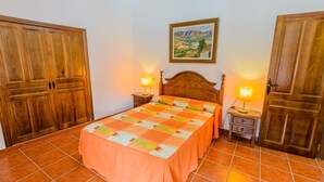 Un dormitorio con cama, dos mesitas de noche, armarios de madera, un cuadro en la pared y suelo de baldosas.