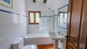 Un baño con inodoro blanco, bañera, cabina de ducha con mampara de vidrio y lavamanos con espejo.