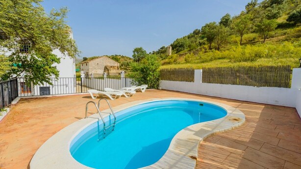Piscina rectangular con escalera, rodeada por un muro blanco y una terraza de madera.