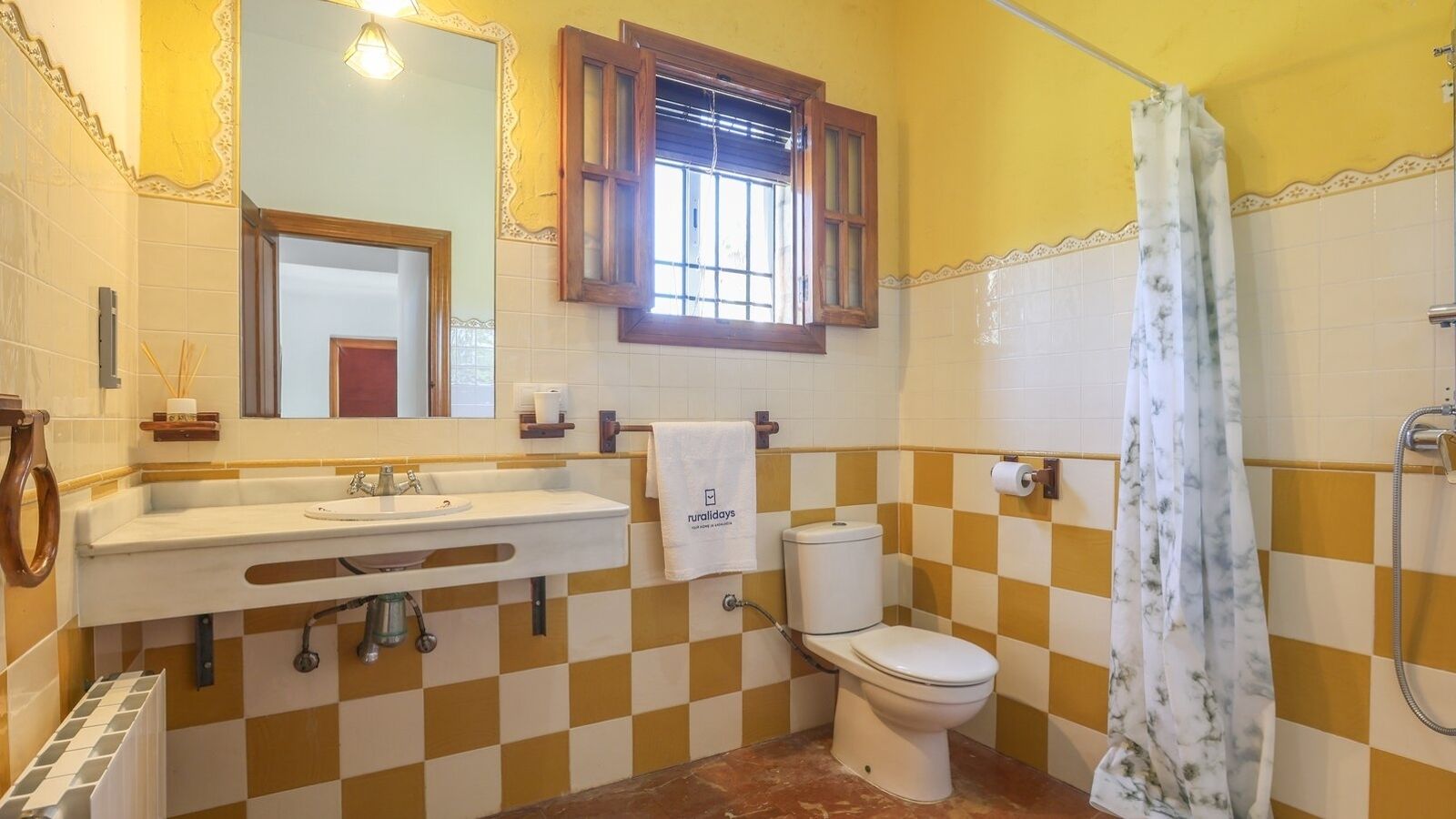 Un baño con piso de baldosas a cuadros, un lavamanos con espejo, un inodoro y una cortina de ducha.