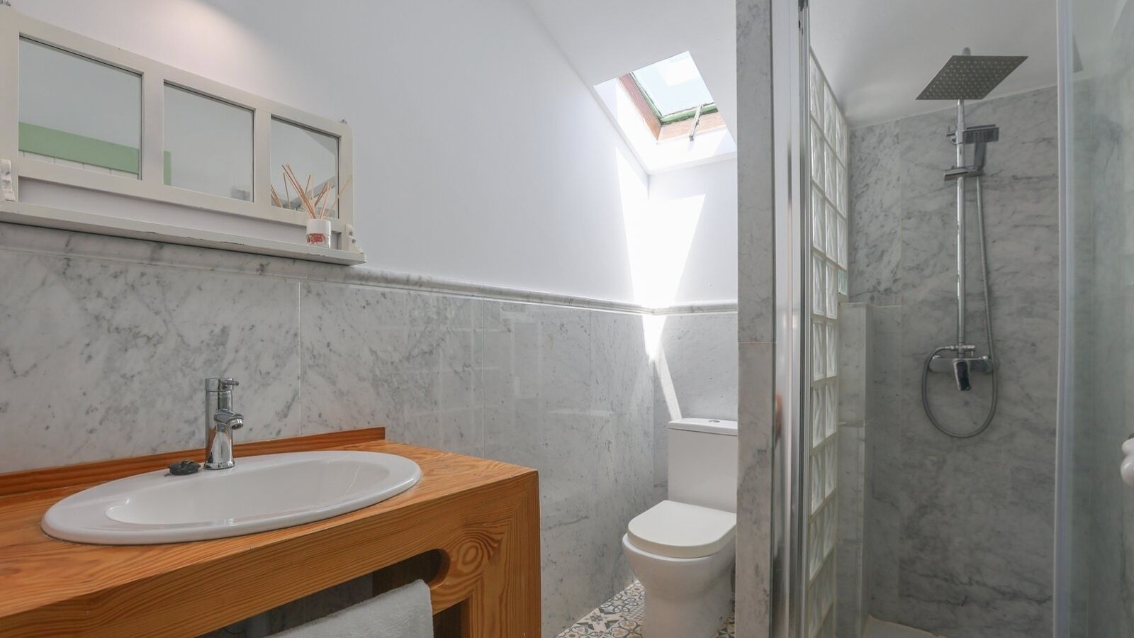 Une salle de bain moderne avec un meuble-lavabo en bois, un lavabo blanc, des toilettes et une douche séparée par une paroi de verre.