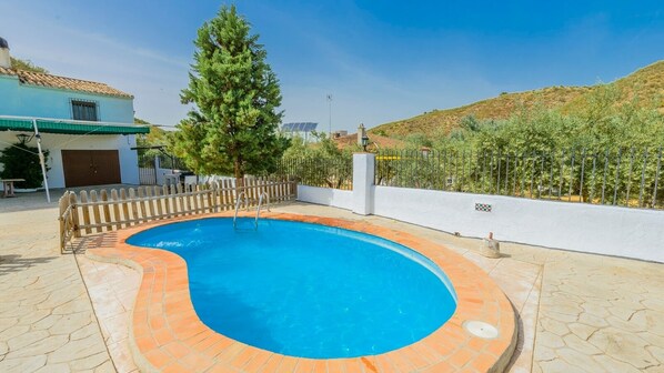 Une piscine avec une terrasse en bois, une clôture en bois et un grand arbre en arrière-plan.