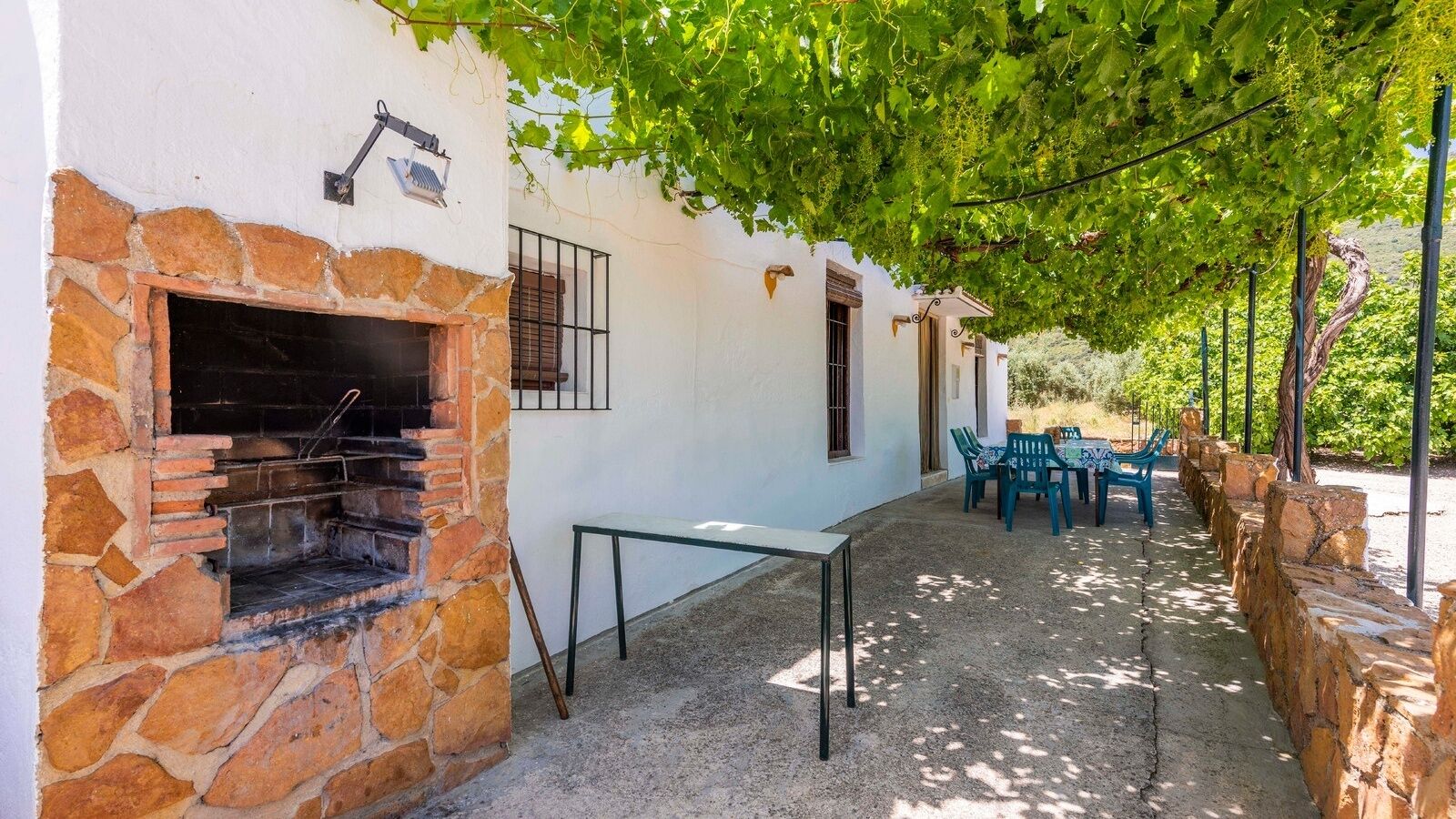 A stone-built outdoor area with a grill, a table, and chairs under a tree.